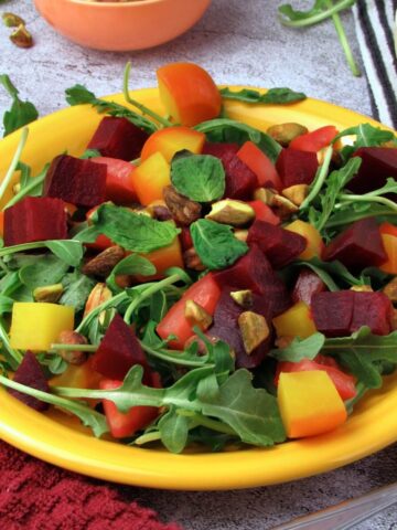 Close up of roasted beet salad with arugula, heirloom tomato, and citrus tahini dressing.