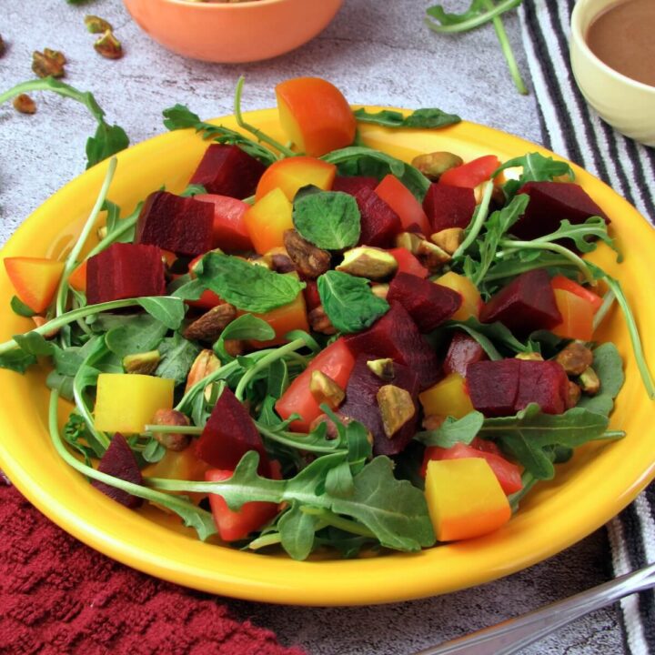 Close up of roasted beet salad with arugula, heirloom tomato, and citrus tahini dressing.