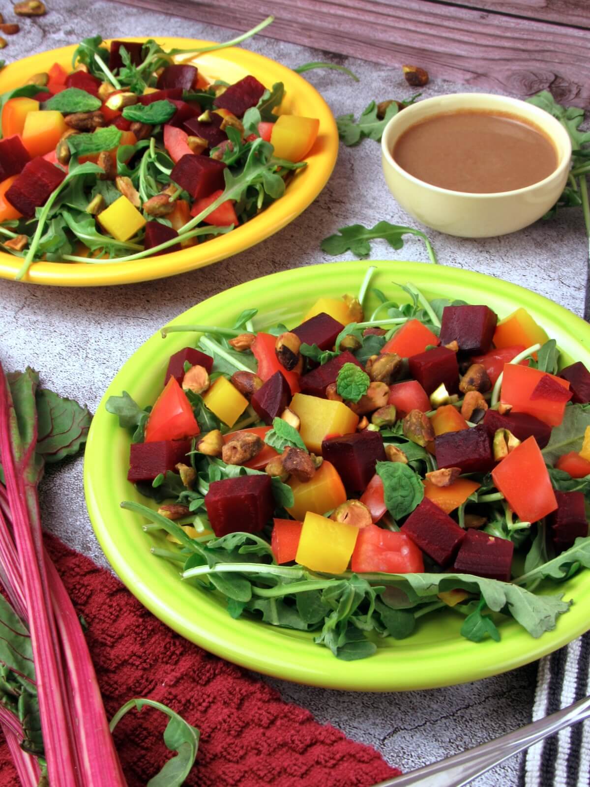 Two plates of summer salad with arugula, roasted red and golden beets, tomato, and a creamy citrus dressing.