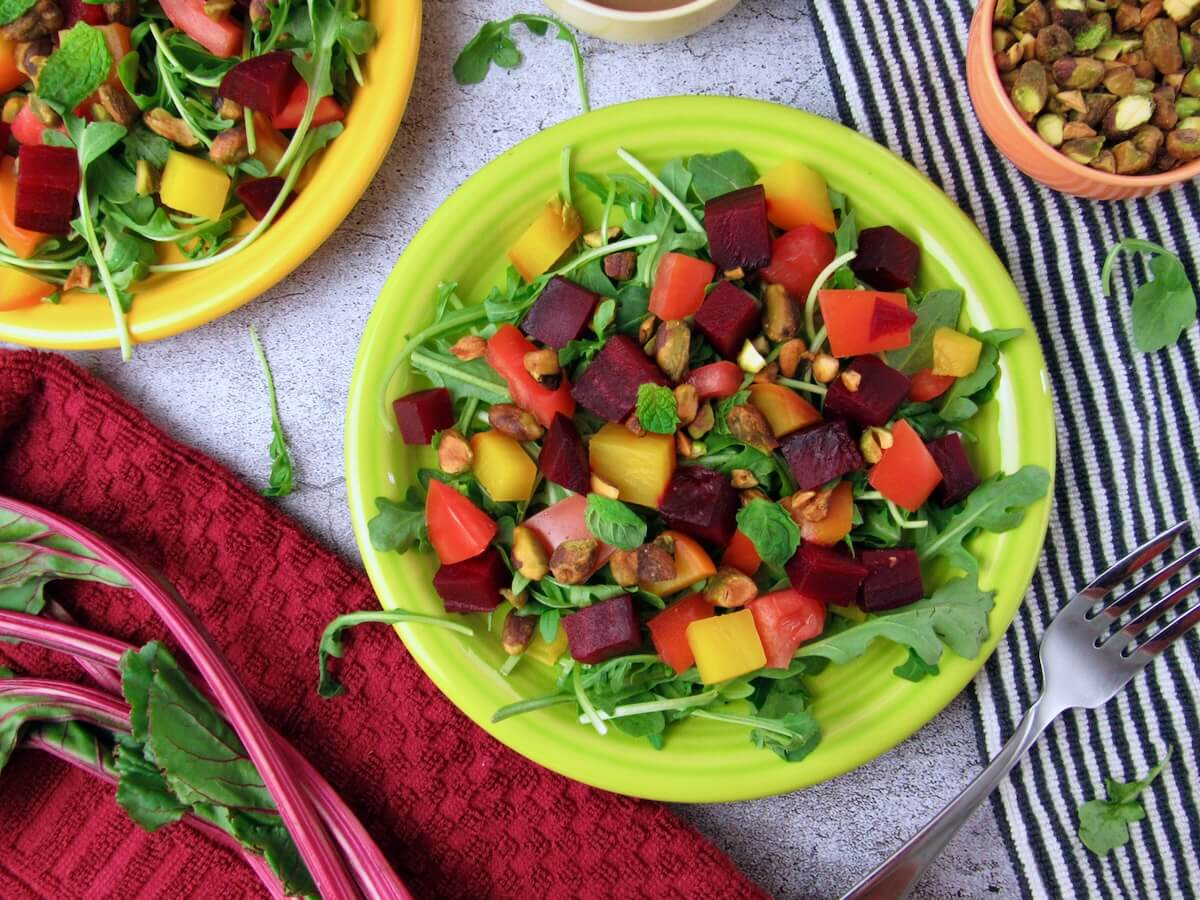 Overhead view of beet and arugula salad with tomatoes, pistachios, mint, and citrus tahini dressing.
