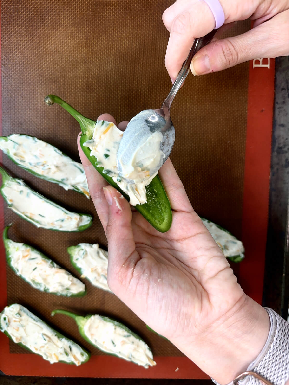Filling jalapeños with vegan cream cheese mixture for a vegan appetizer.
