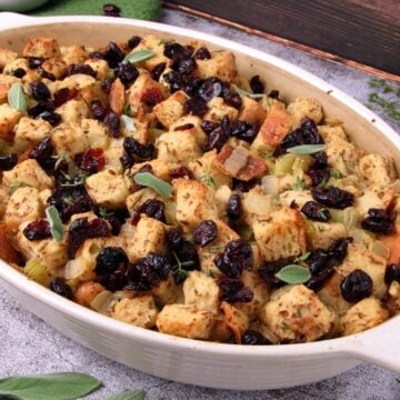 Vegan sourdough Thanksgiving stuffing with fresh herbs and dried cranberries, served in a casserole dish.