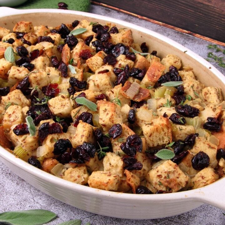 Vegan sourdough Thanksgiving stuffing with fresh herbs and dried cranberries, served in a casserole dish.